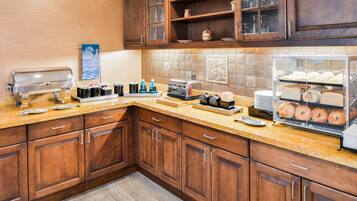A kitchen with wooden cabinets, a coffee station, and a display case with pastries.