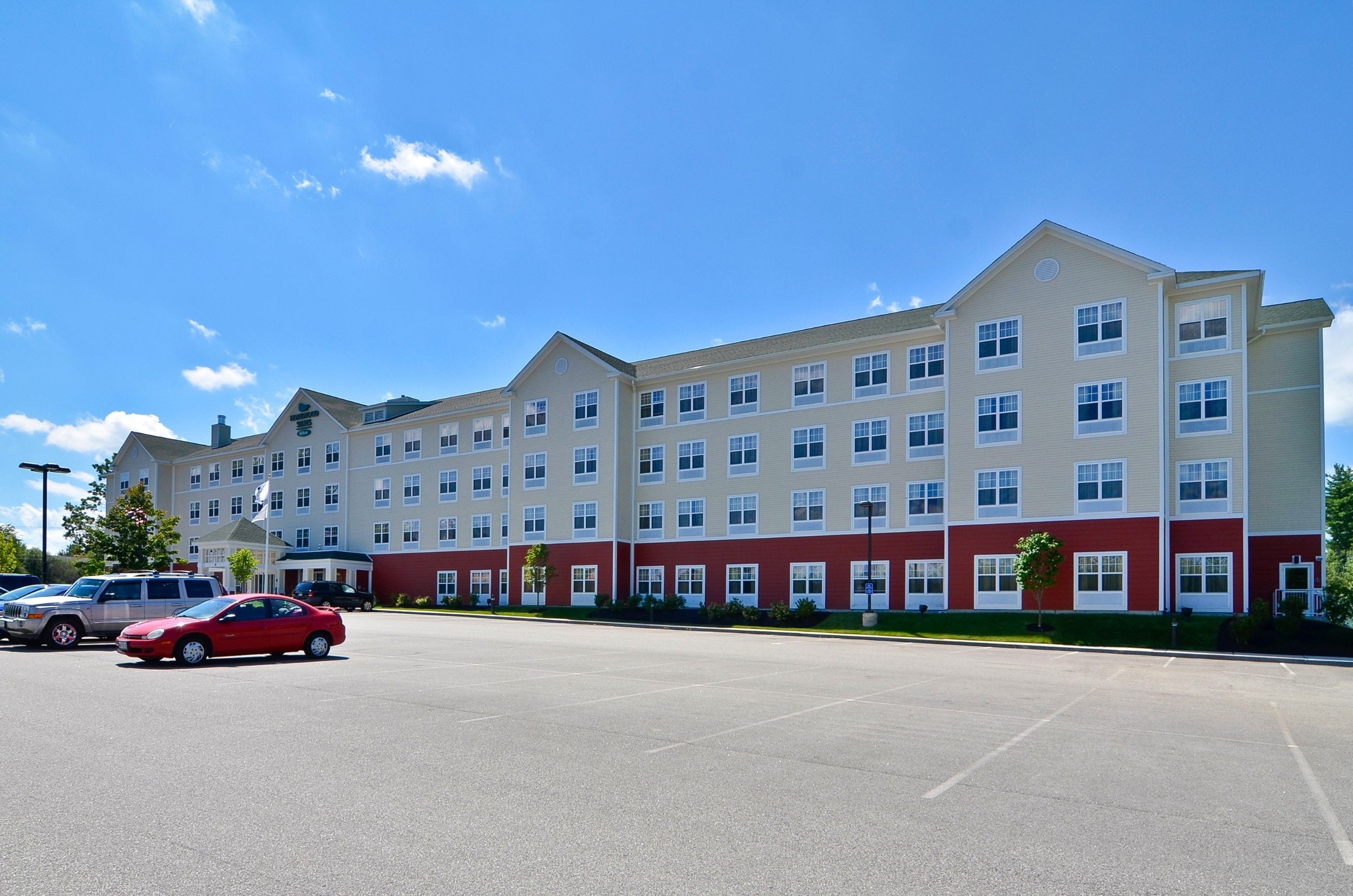 Un hôtel à plusieurs étages, doté d’une façade rouge et beige, d’un parking et surplombant un ciel d’un bleu limpide.