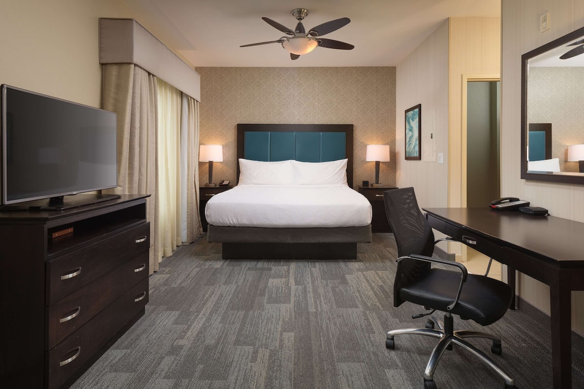 A hotel room with a bed, a desk, a chair, a television, and a ceiling fan.