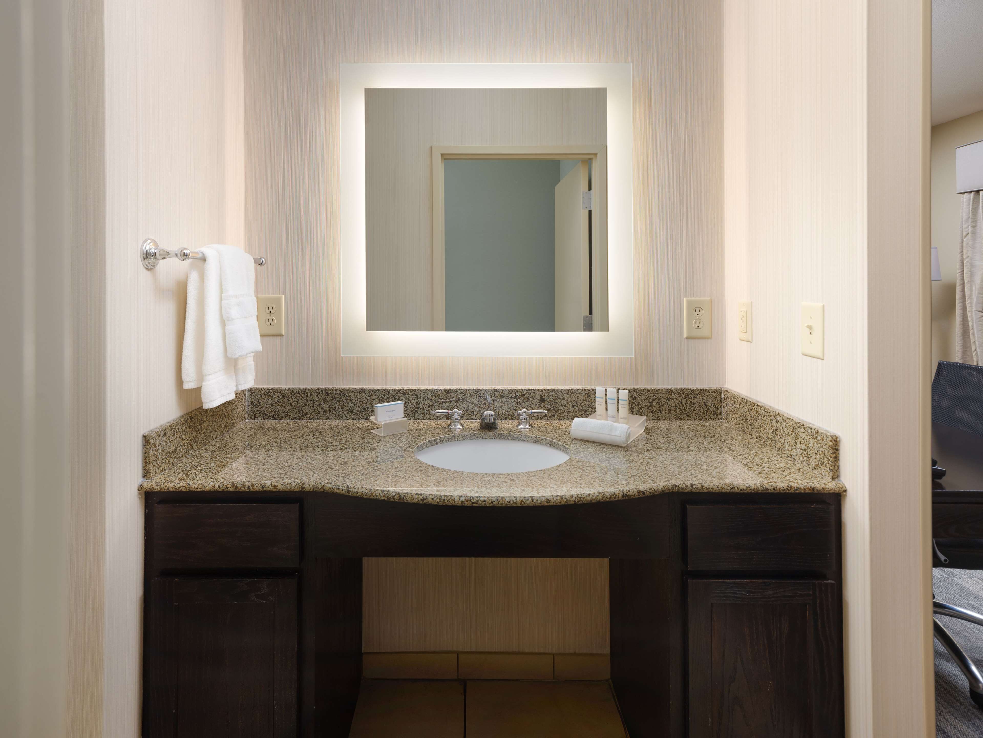 A bathroom with a granite countertop sink, dark wooden cabinets, a large mirror, and a towel rack.