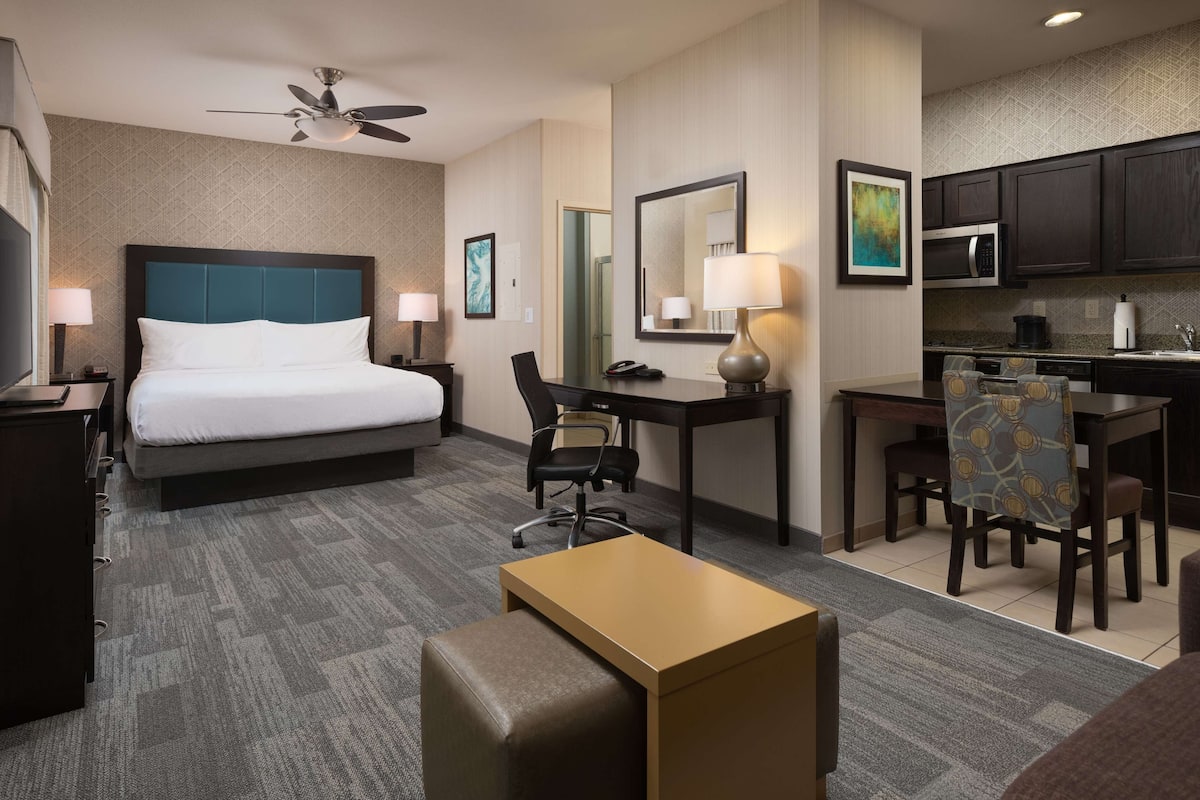 A hotel room with a bed, desk, office chair, kitchenette, and a small seating area.