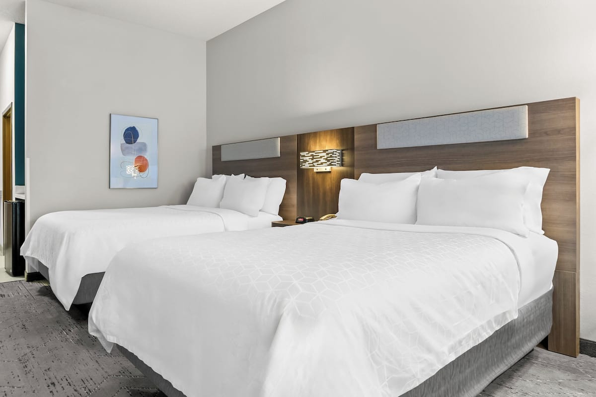 A hotel room with two beds, a modern headboard, a wall-mounted light fixture, and a framed abstract painting.