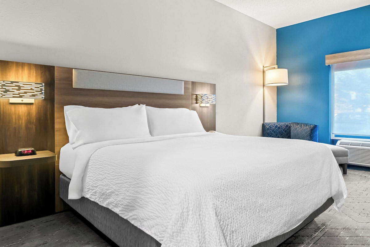 Een moderne hotelkamer met een groot bed, een nachtkastje met een klok, een wandlamp en een raam met uitzicht.