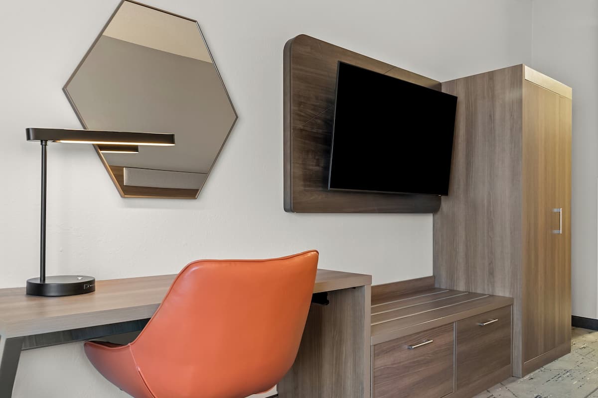 A modern room with a desk, a leather chair, a wall-mounted TV, and a large mirror.