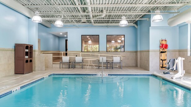 An indoor swimming pool with a bar area, seating, and a lifeguard stand. - Holiday Inn Express Hotel & Suites Detroit-Novi by IHG (Novi)