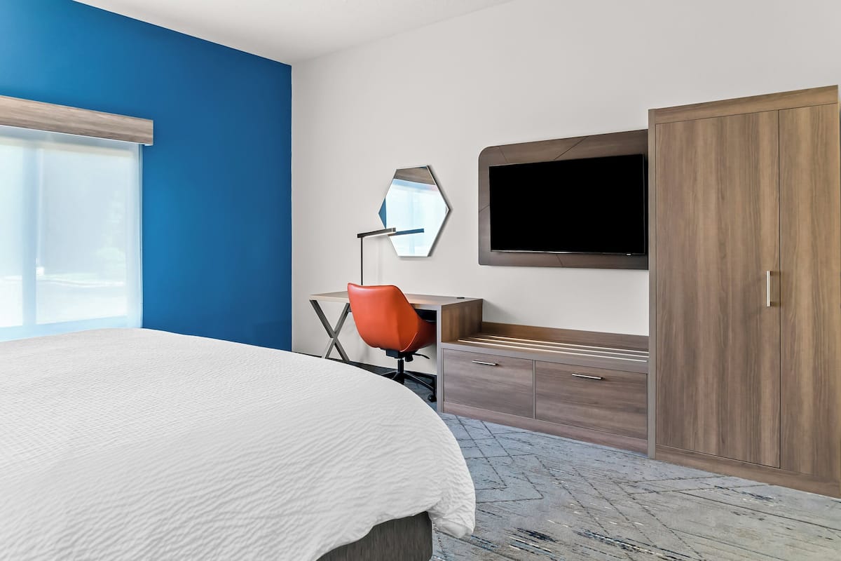 A hotel room with a large bed, a desk with a chair, a TV, and a wardrobe.