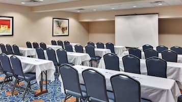 A conference room with rows of tables and chairs, a projector screen, and a carpeted floor.