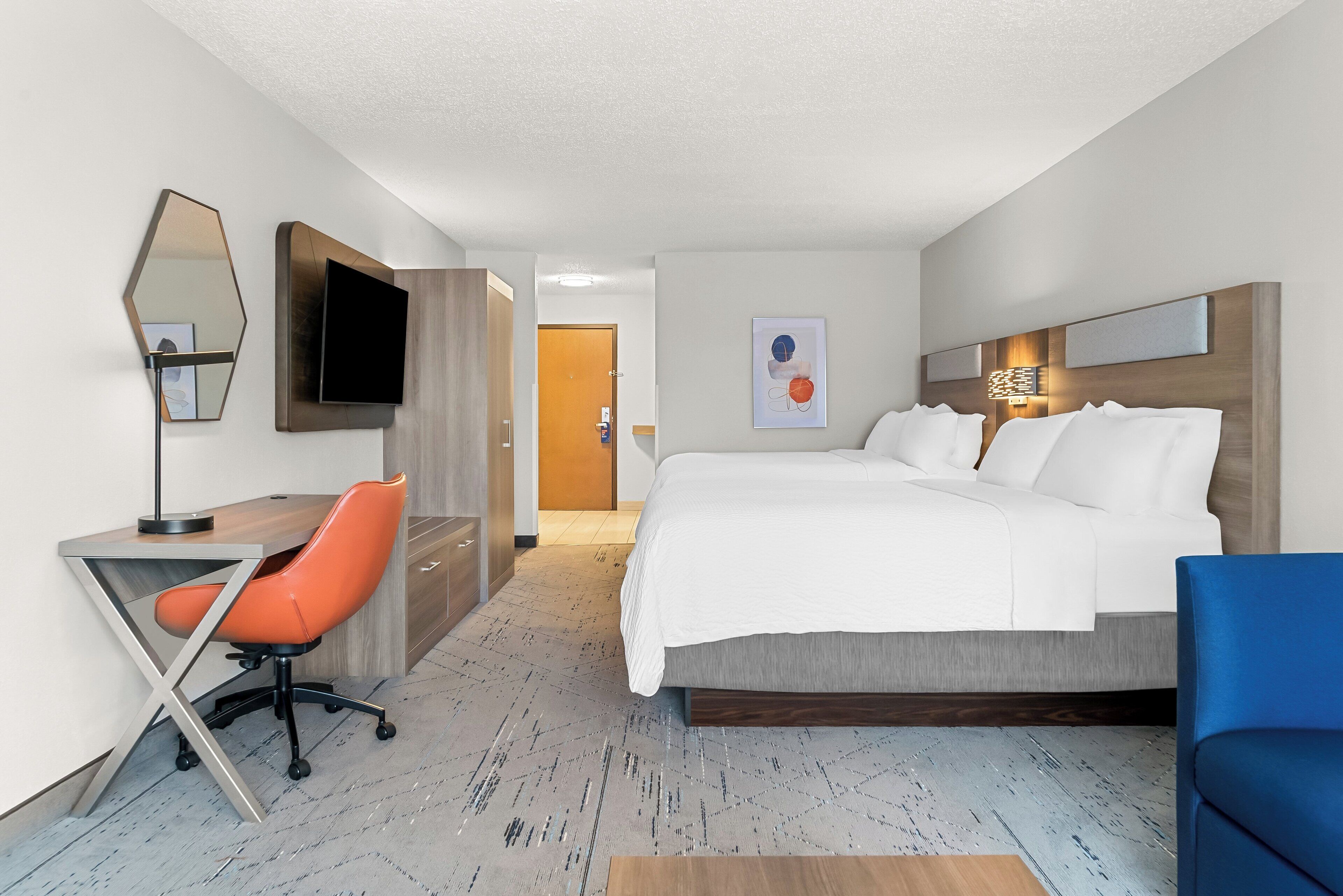 Una habitación de hotel moderna con cama, escritorio, silla, televisor y espejo.