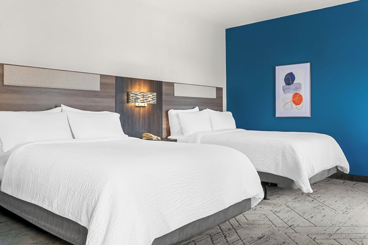 A hotel room with two beds, a nightstand, a wall-mounted light, and a framed abstract painting.
