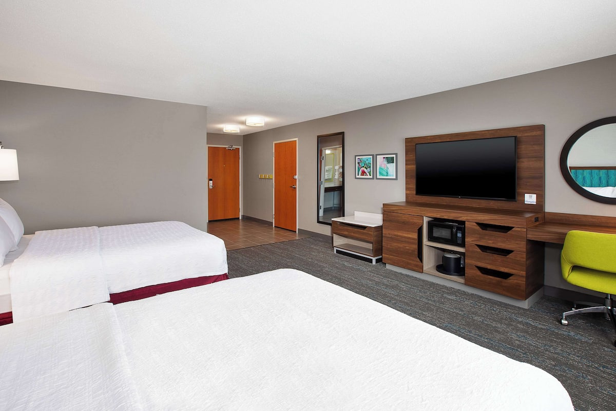 A hotel room with two beds, a desk, a chair, a TV, and a mirror.