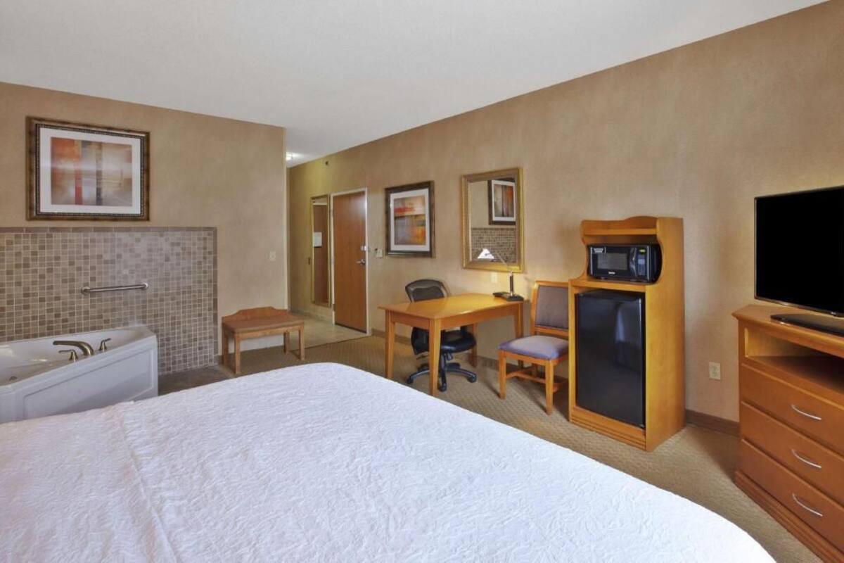 A hotel room with a bed, a desk, a chair, a television, a microwave, and a small table.