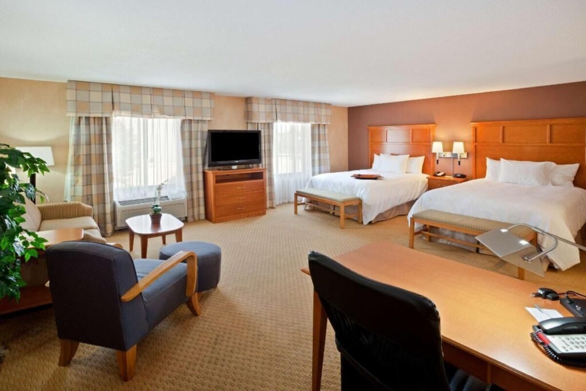 A hotel room with two beds, a TV, a desk with a chair, a small table, and a lamp.