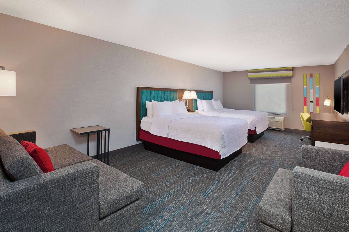 A hotel room with two beds, a sofa, a small table, and a TV.