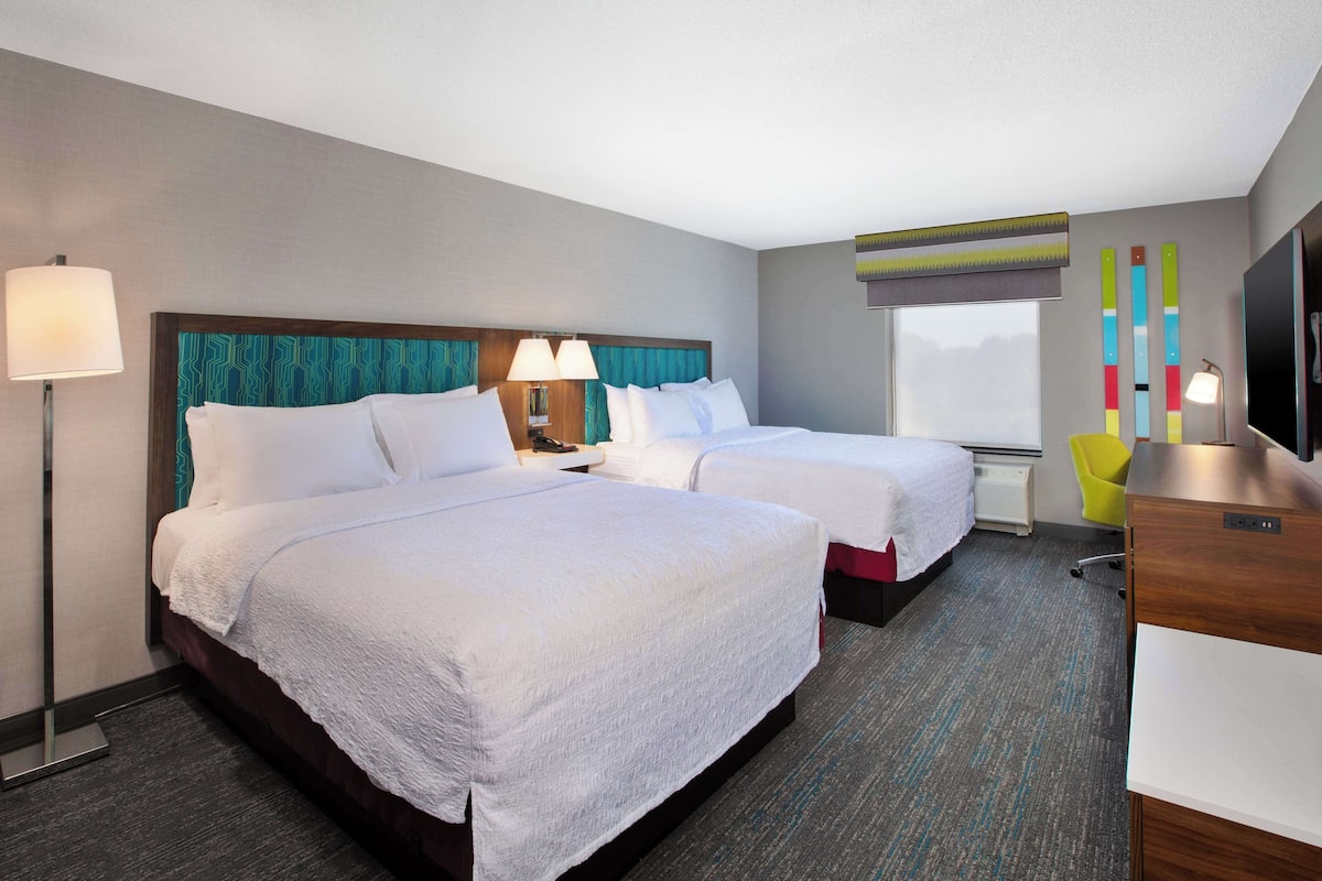 A hotel room with two beds, a desk, a chair, a TV, and a window.