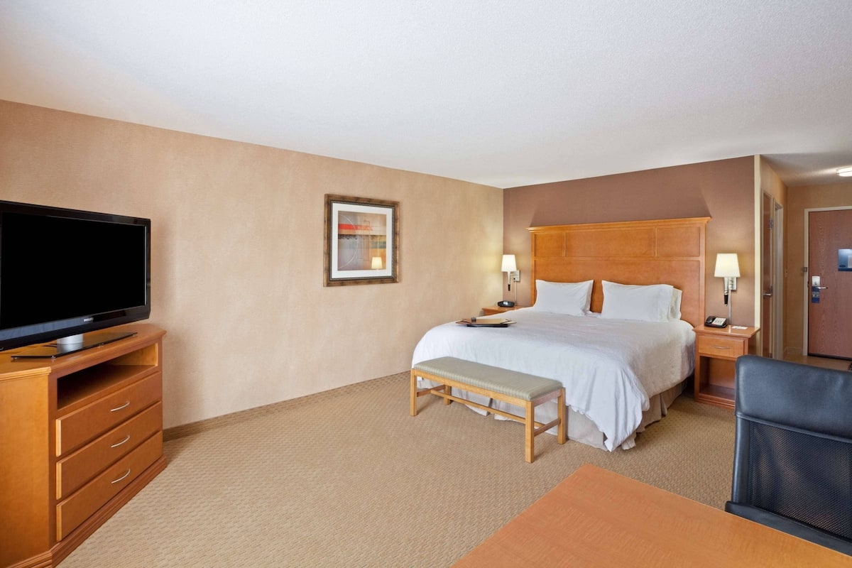A hotel room with a bed, bedside tables, a television, a bench, and a desk.
