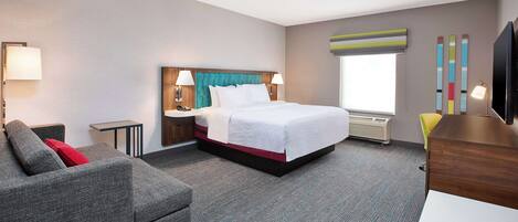 A hotel room with a bed, a sofa, a desk, and a television.