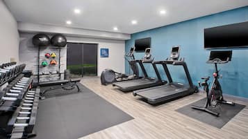 Un gimnasio con cintas de correr, bicicletas estáticas y una máquina de remo.