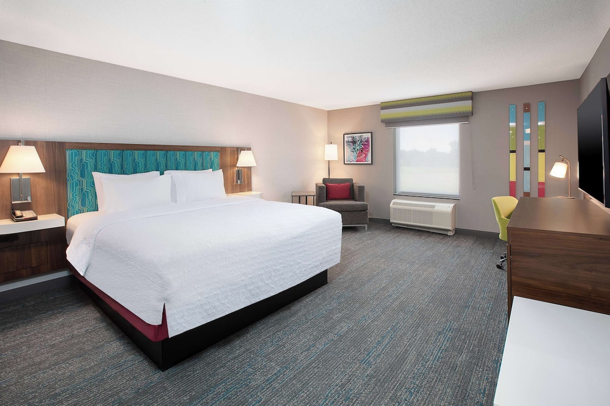A hotel room with a large bed, a desk, a chair, a TV, and a window.