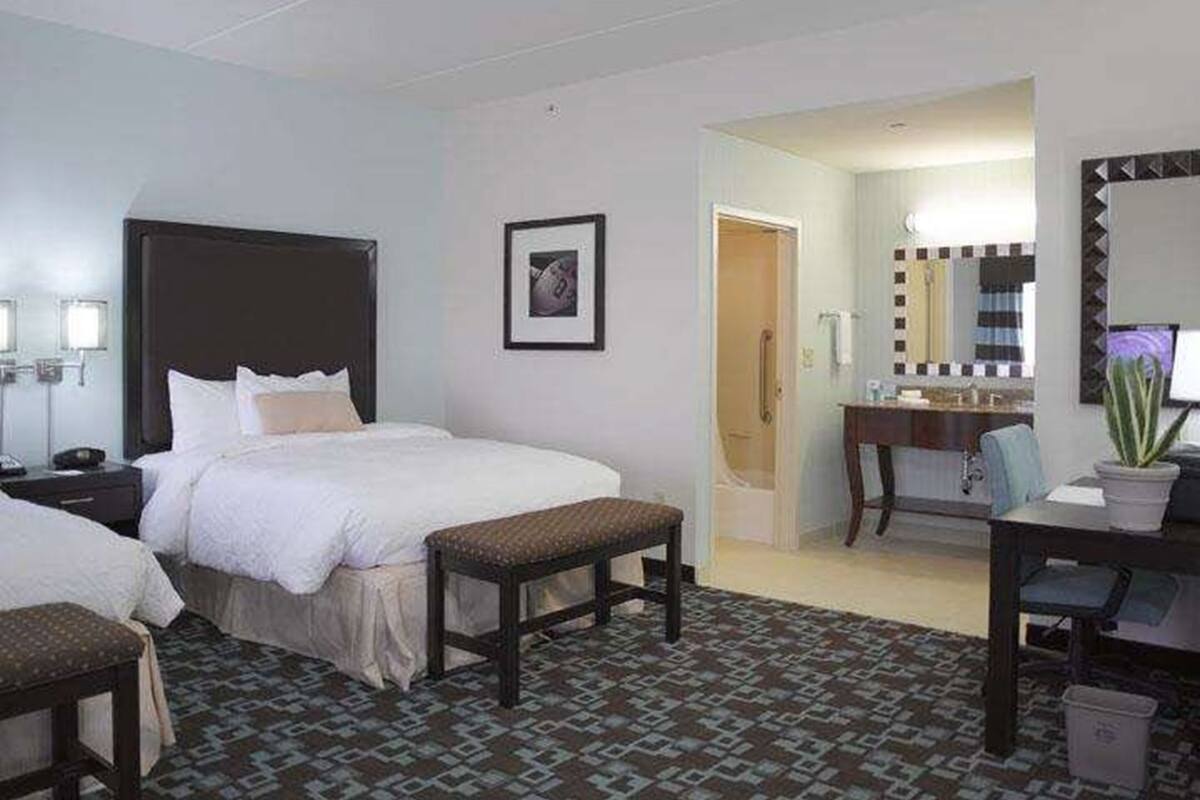A hotel room with a bed, bedside table, chair, desk, and a bathroom visible through an open door.