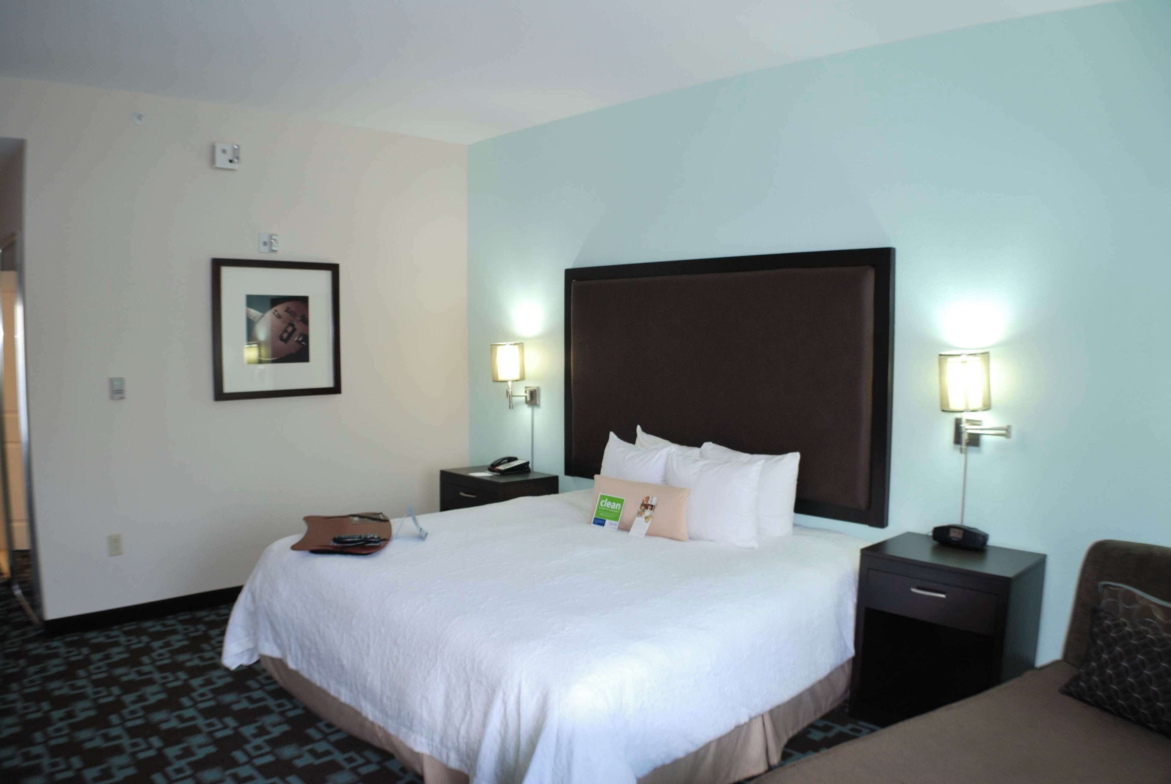 Ein Hotelzimmer mit einem großen Bett, zwei Nachttischen, einem Schminktisch, einem Sessel und einem gerahmten Bild an der Wand.
