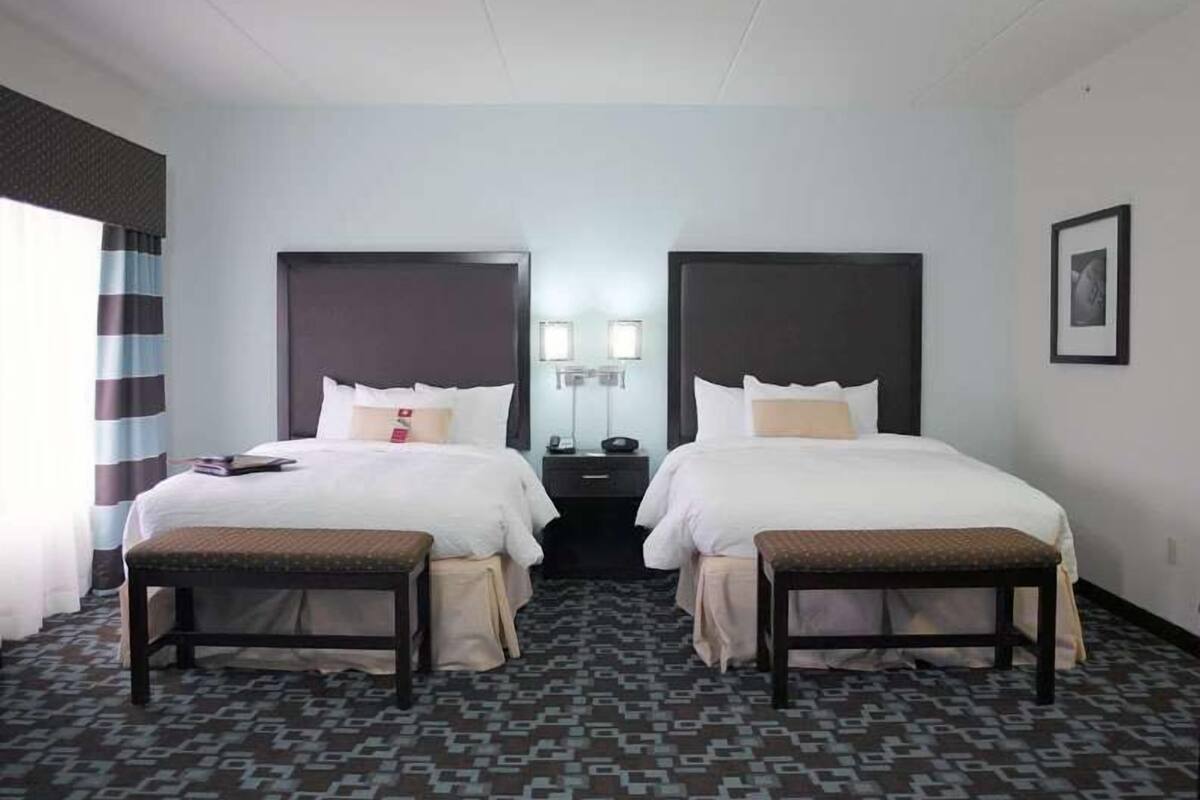 A hotel room with two beds, a bedside table, a lamp, and a patterned carpet.