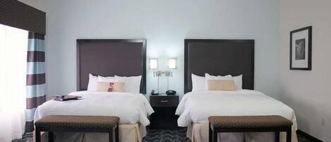 A hotel room with two beds, a bedside table, a lamp, and a patterned carpet.