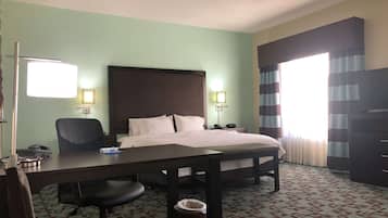 A hotel room with a bed, desk, chair, and a trash bin.