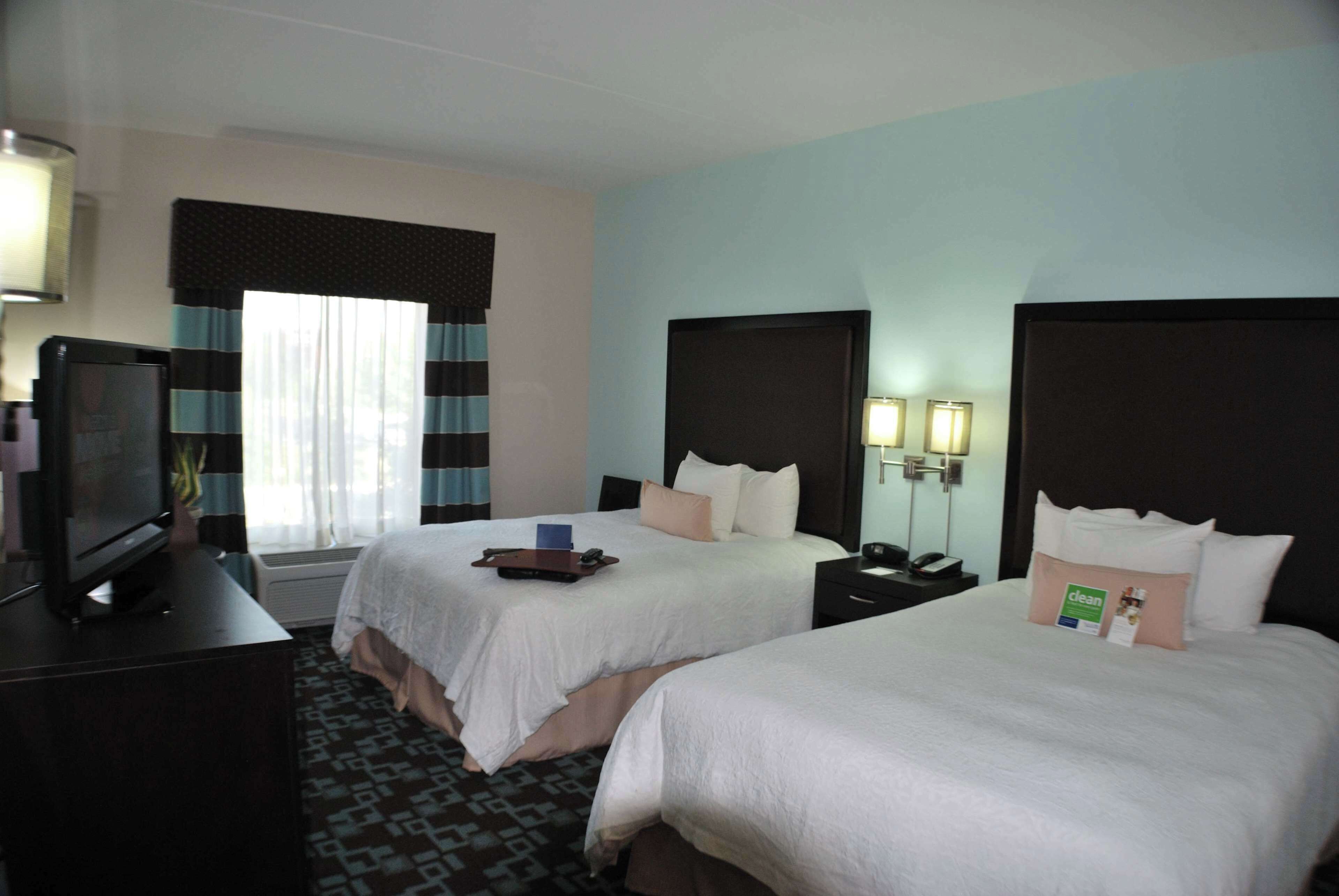 A hotel room with two beds, a TV, a desk, and a window with curtains.