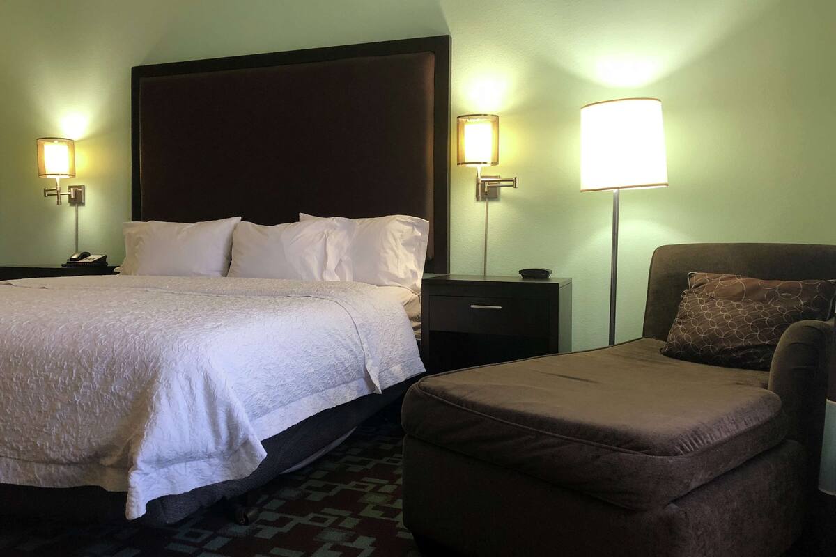 A hotel room with a large bed, two bedside tables with lamps, a chair, and a patterned rug.