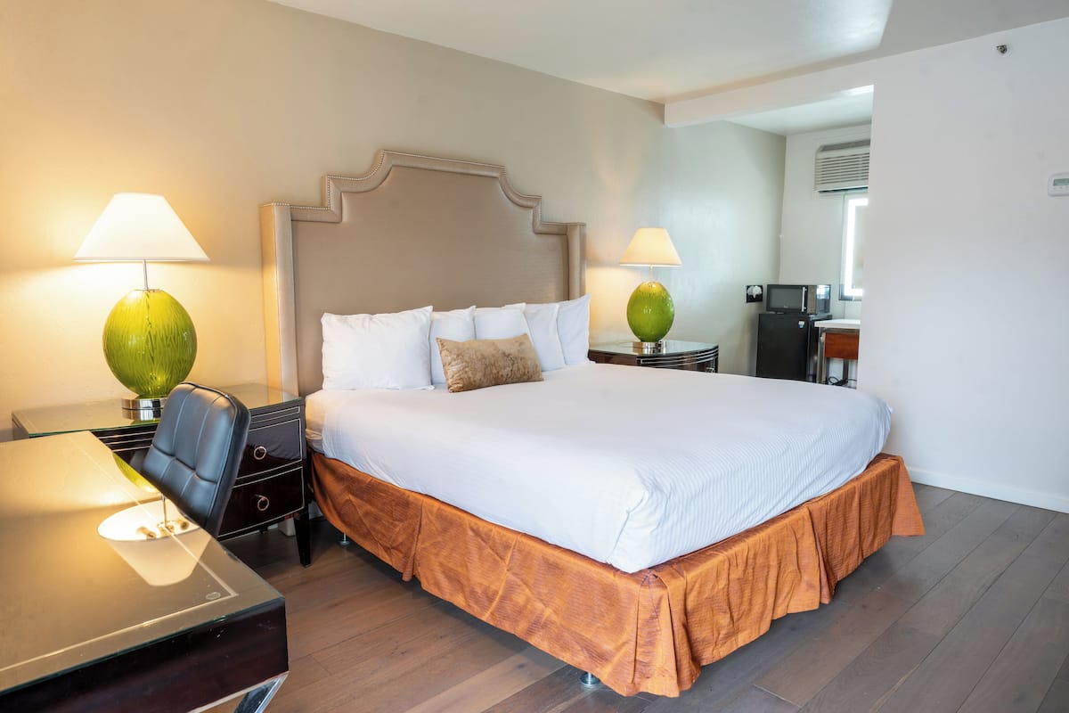 A hotel room with a large bed, two bedside tables with lamps, a desk, and a chair.