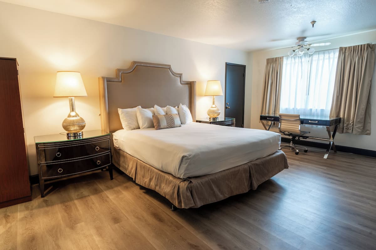 A hotel room with a large bed, two bedside tables with lamps, a desk with a chair, and a ceiling fan.