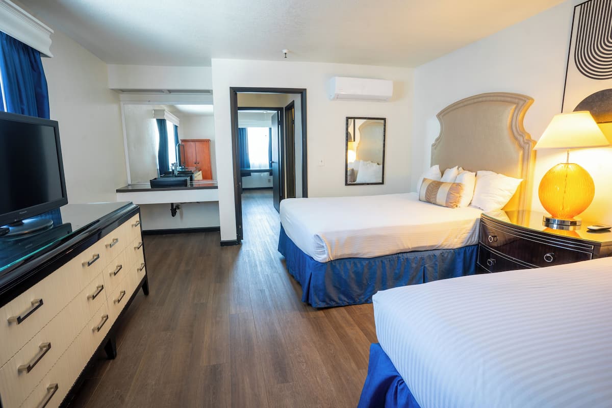 A hotel room with two beds, a TV, a dresser, and a bathroom visible through an open door.