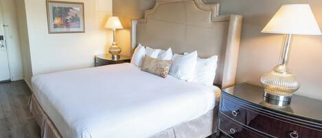 Una cama bien hecha con cabecera, dos mesitas de noche con lámparas y suelo de madera.