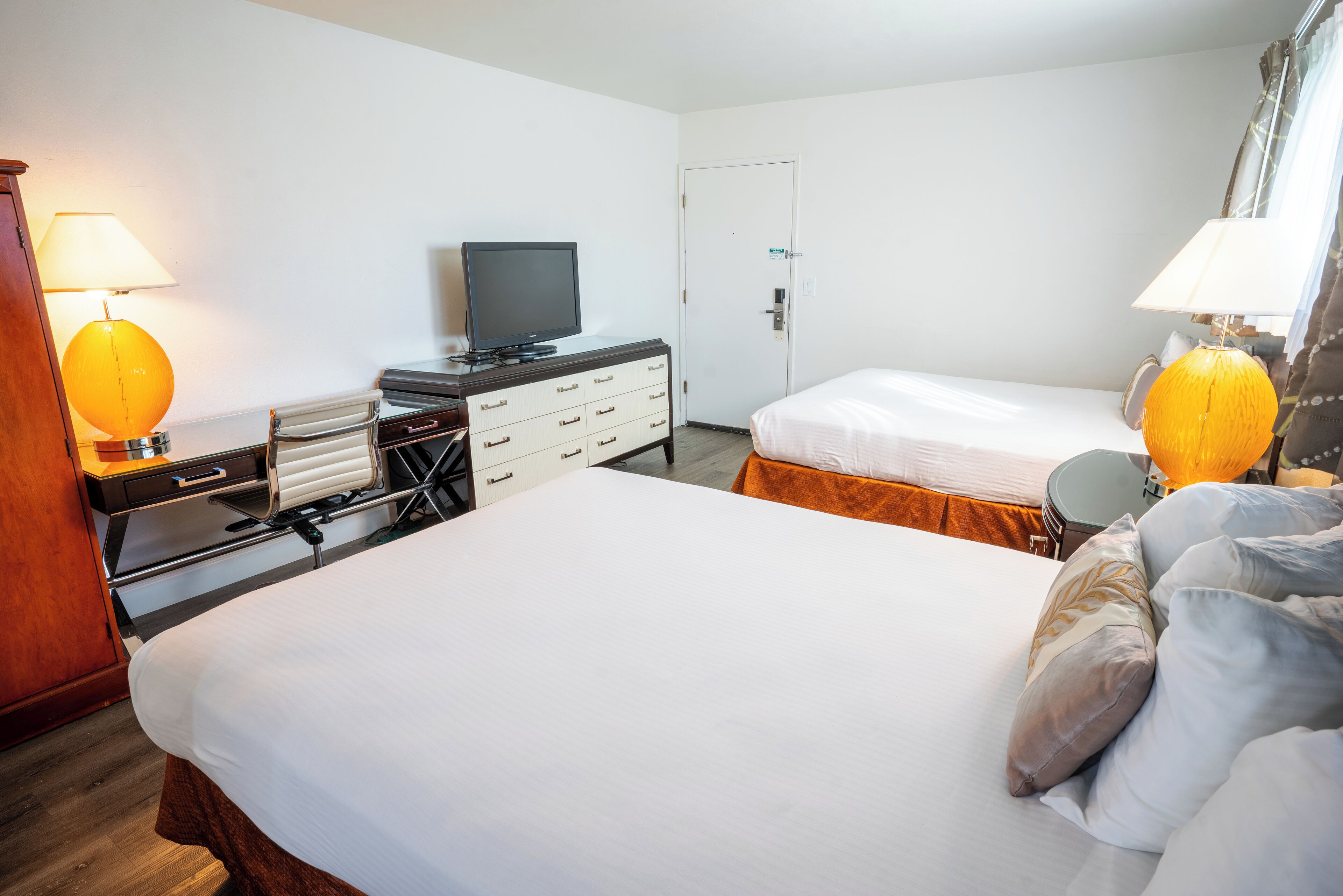 Une chambre d’hôtel avec deux lits, une télévision, un bureau avec une lampe et une commode.