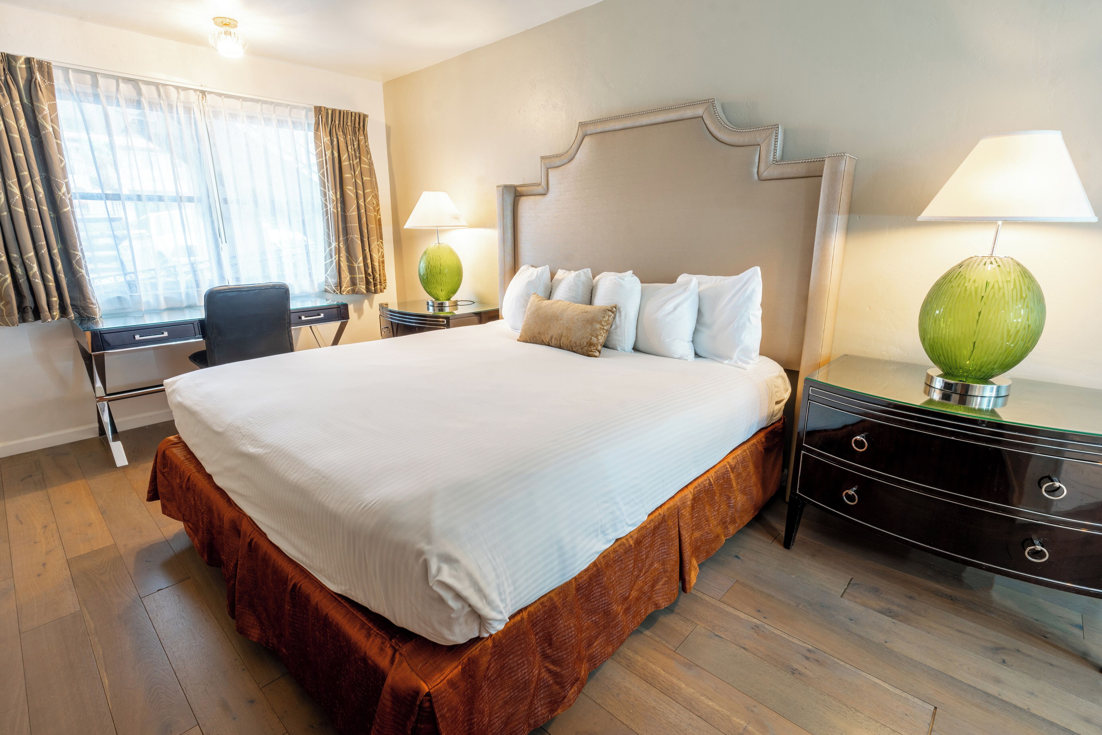 A hotel room with a large bed, a desk, and a chair. There are two lamps on the nightstands.