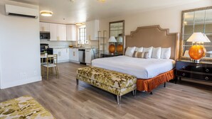A hotel room with a bed, bedside table, lamp, and a small kitchenette.