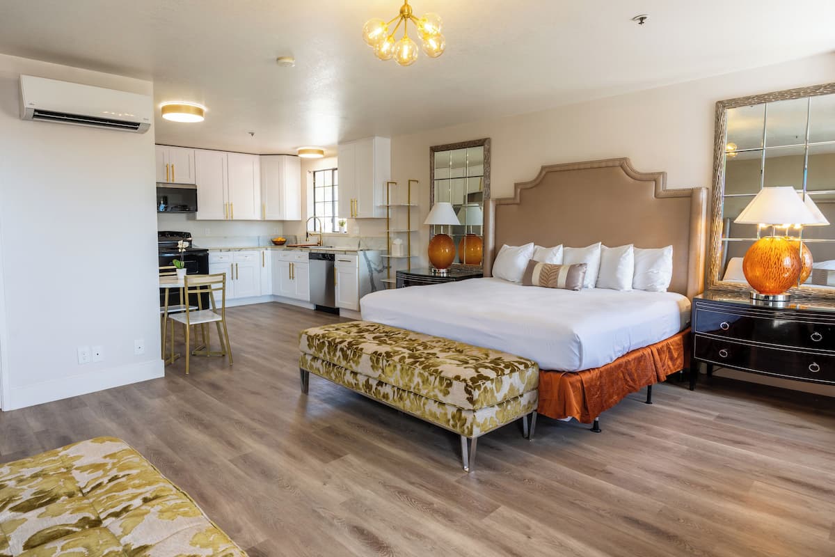 A hotel room with a bed, bedside table, lamp, and a small kitchenette.