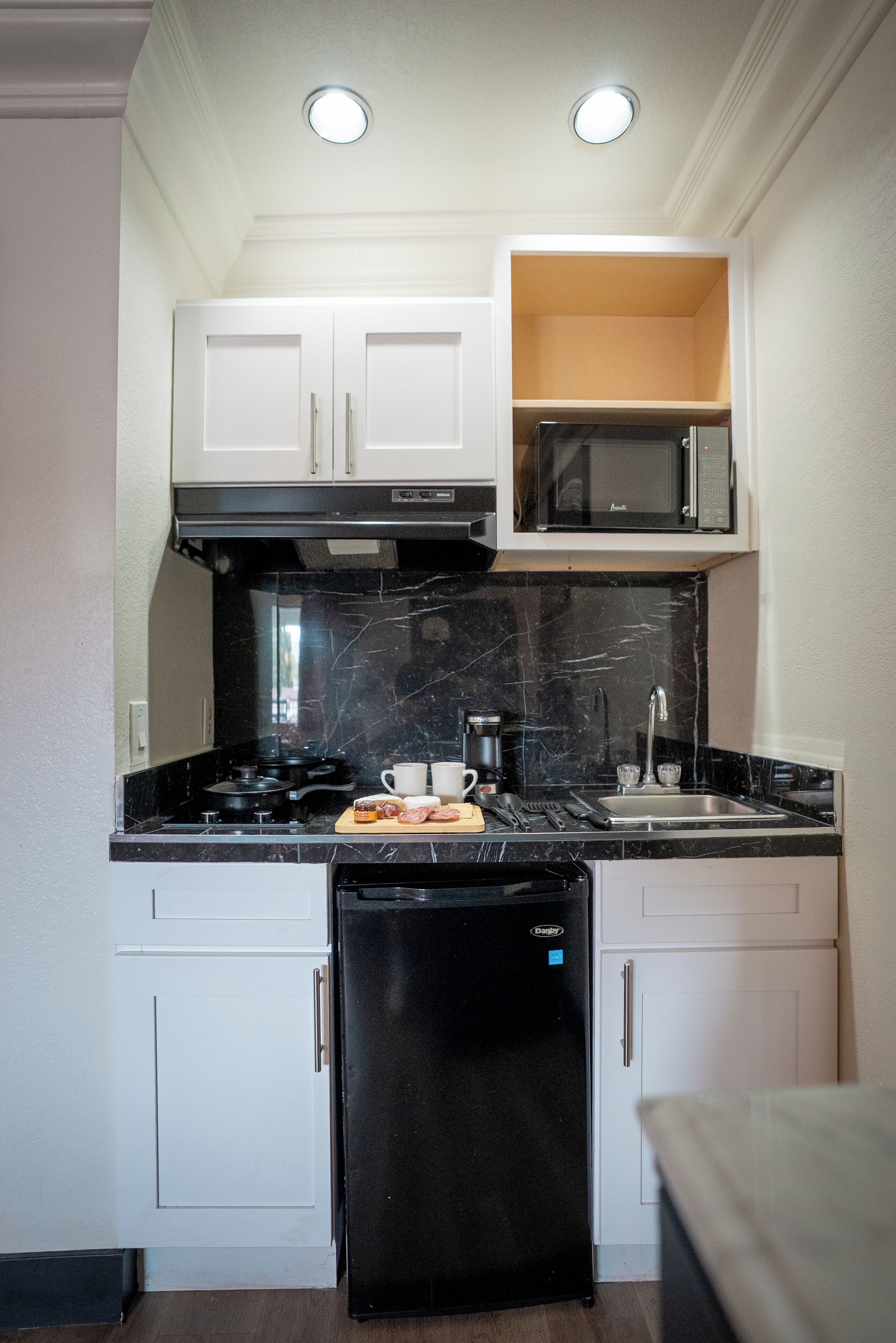 Uma cozinha compacta com armários brancos, uma geladeira preta, micro-ondas e fogão.