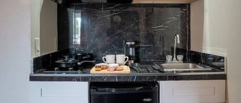 Uma cozinha compacta com armários brancos, uma geladeira preta, micro-ondas e fogão.