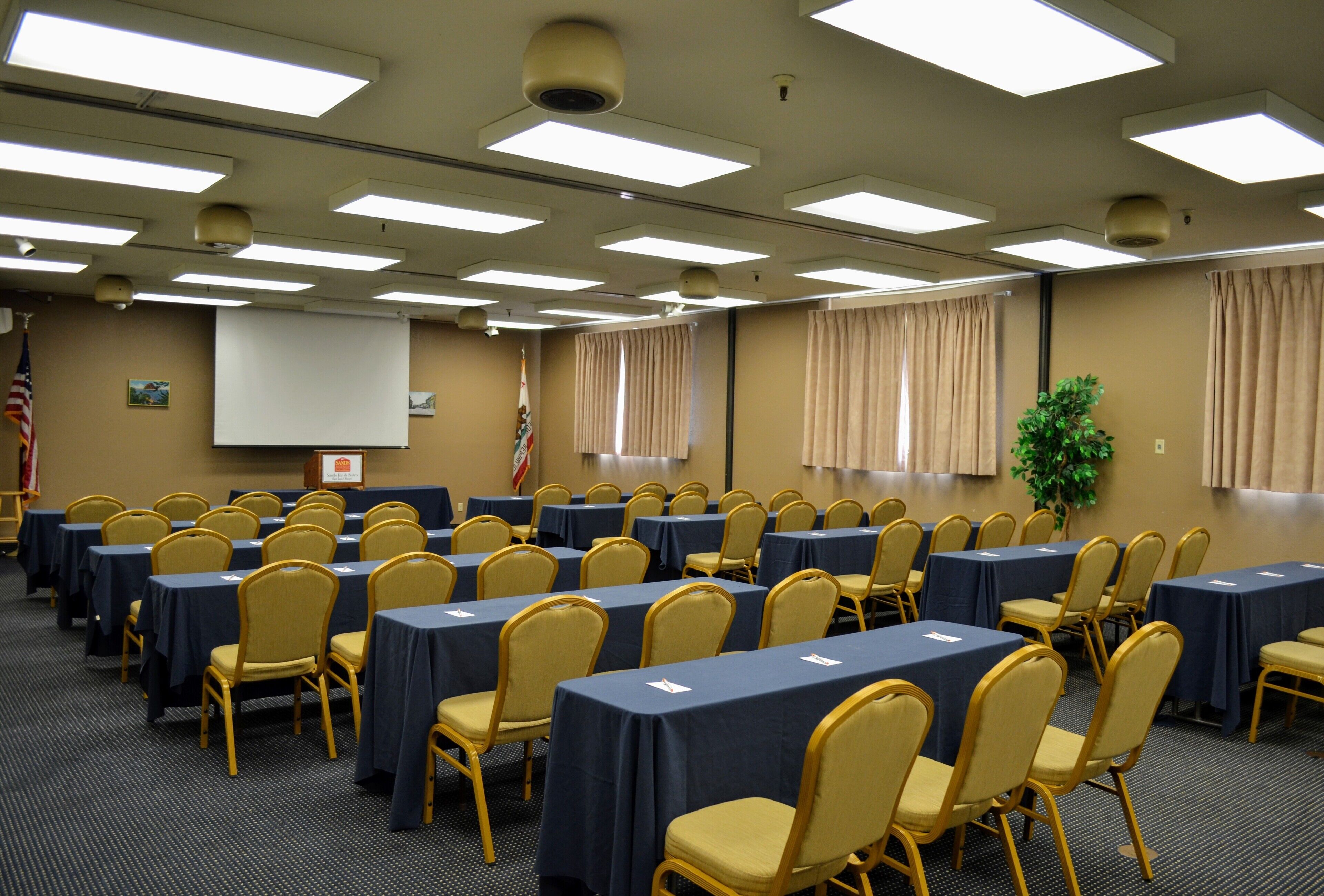 Una sala de conferències amb files de taules i cadires, una pantalla de projector i una bandera dels Estats Units.