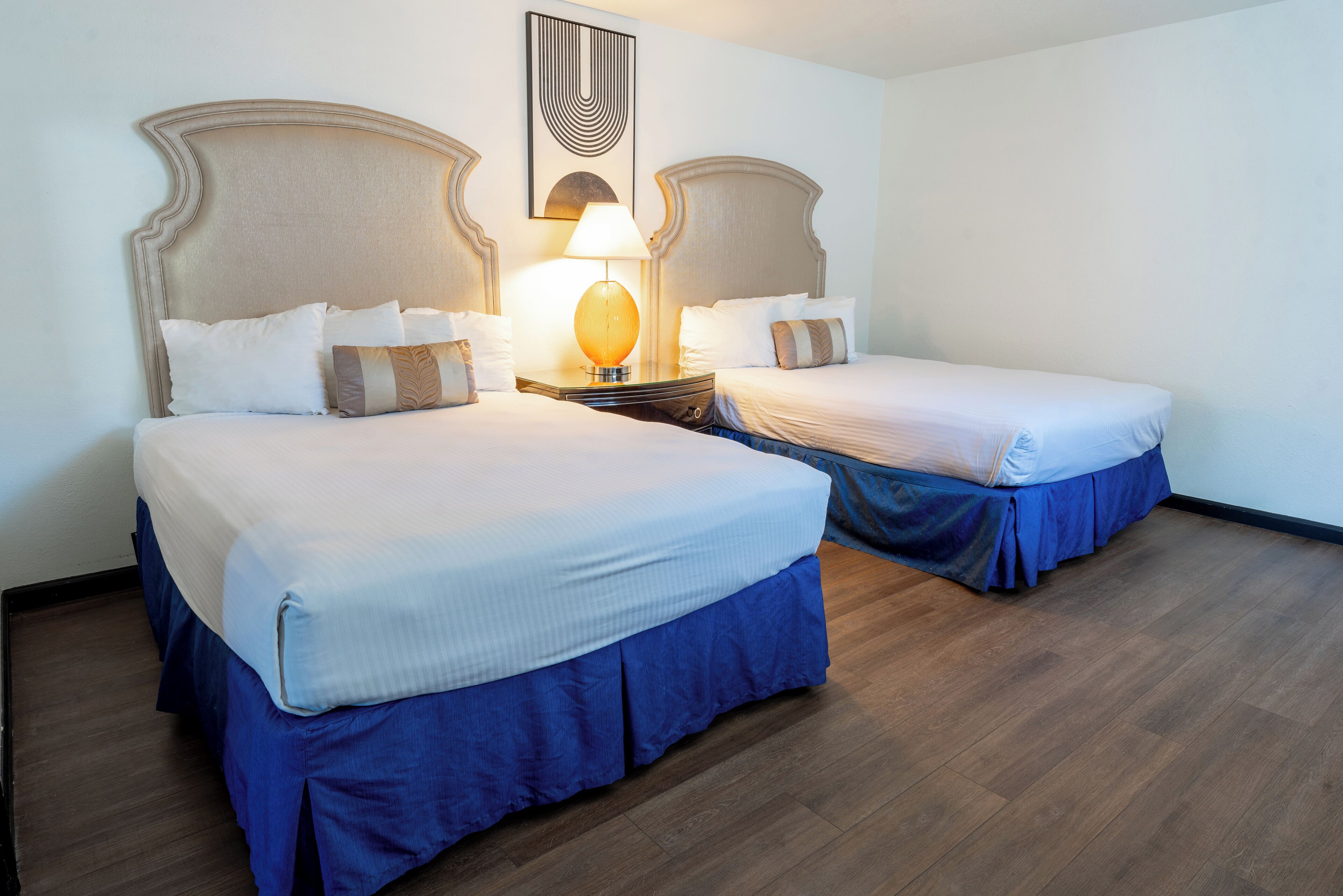 Een hotelkamer met twee bedden, elk met een hoofdeinde, een nachtkastje met een lamp en een aan de muur hangend kunstwerk.