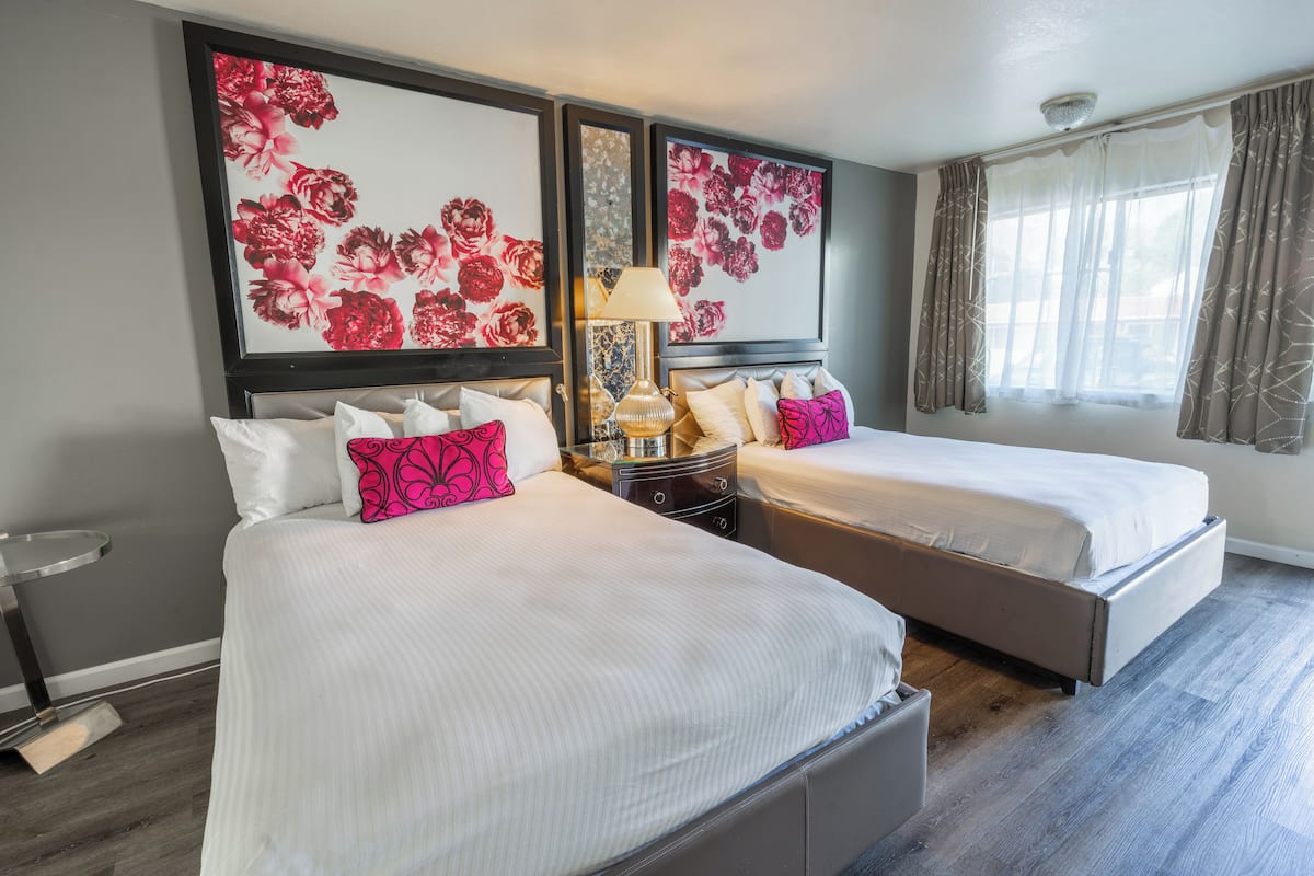 A hotel room with two beds, a bedside table with a lamp, and floral artwork on the walls.