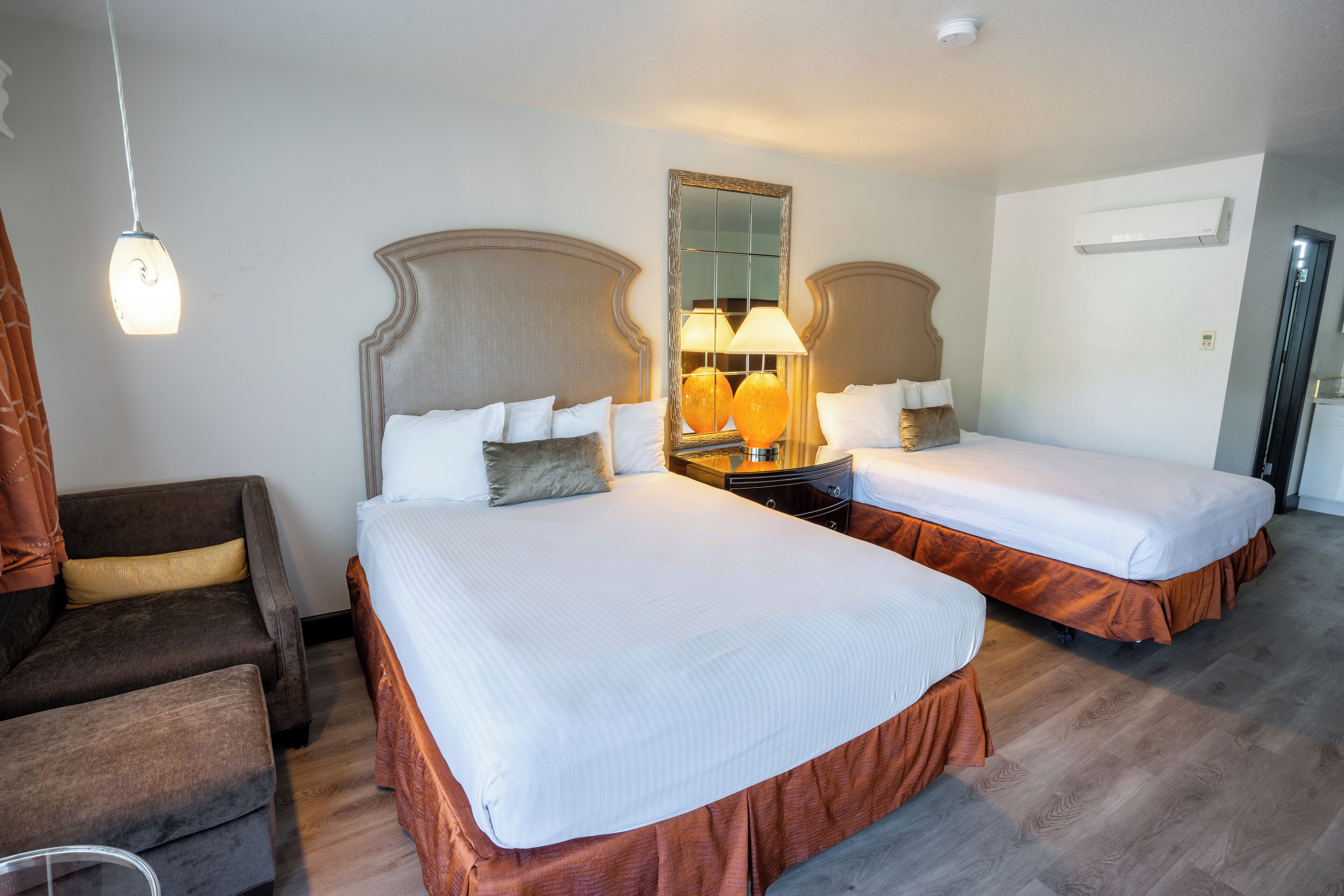 A hotel room with two beds, a sofa, a mirror, and a lamp.