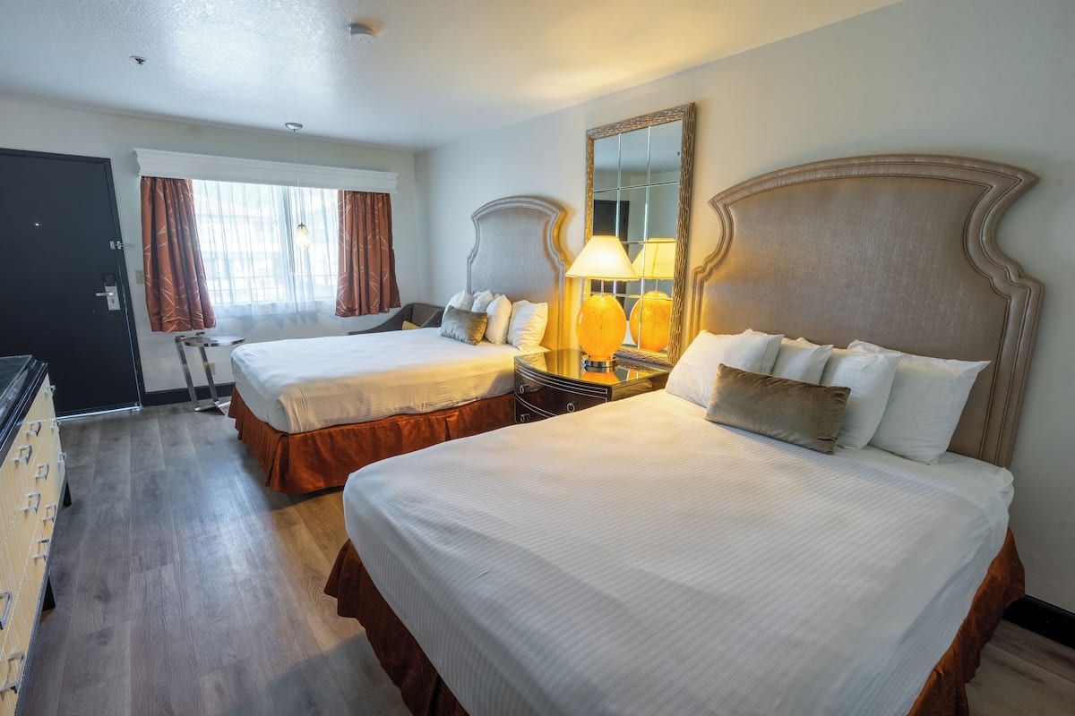 A hotel room with two beds, a large mirror, and a nightstand with lamps.