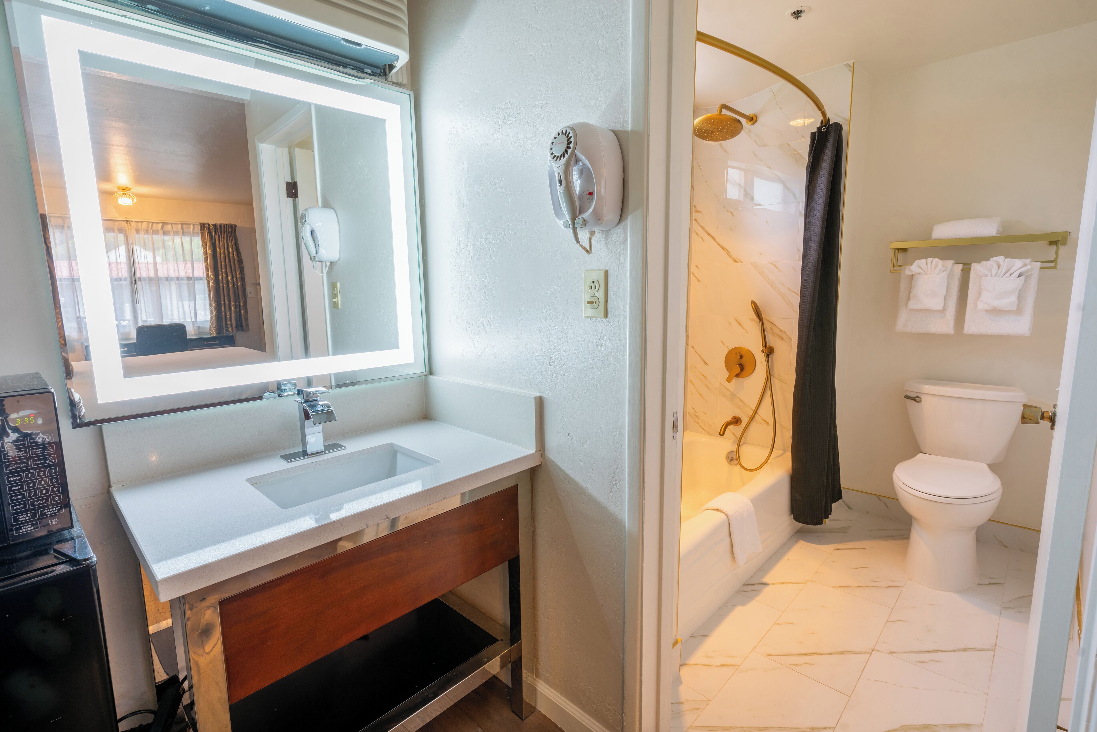 A bathroom with a white sink, mirror, and toilet. There is a shower with a curved glass door and a towel rack with towels.