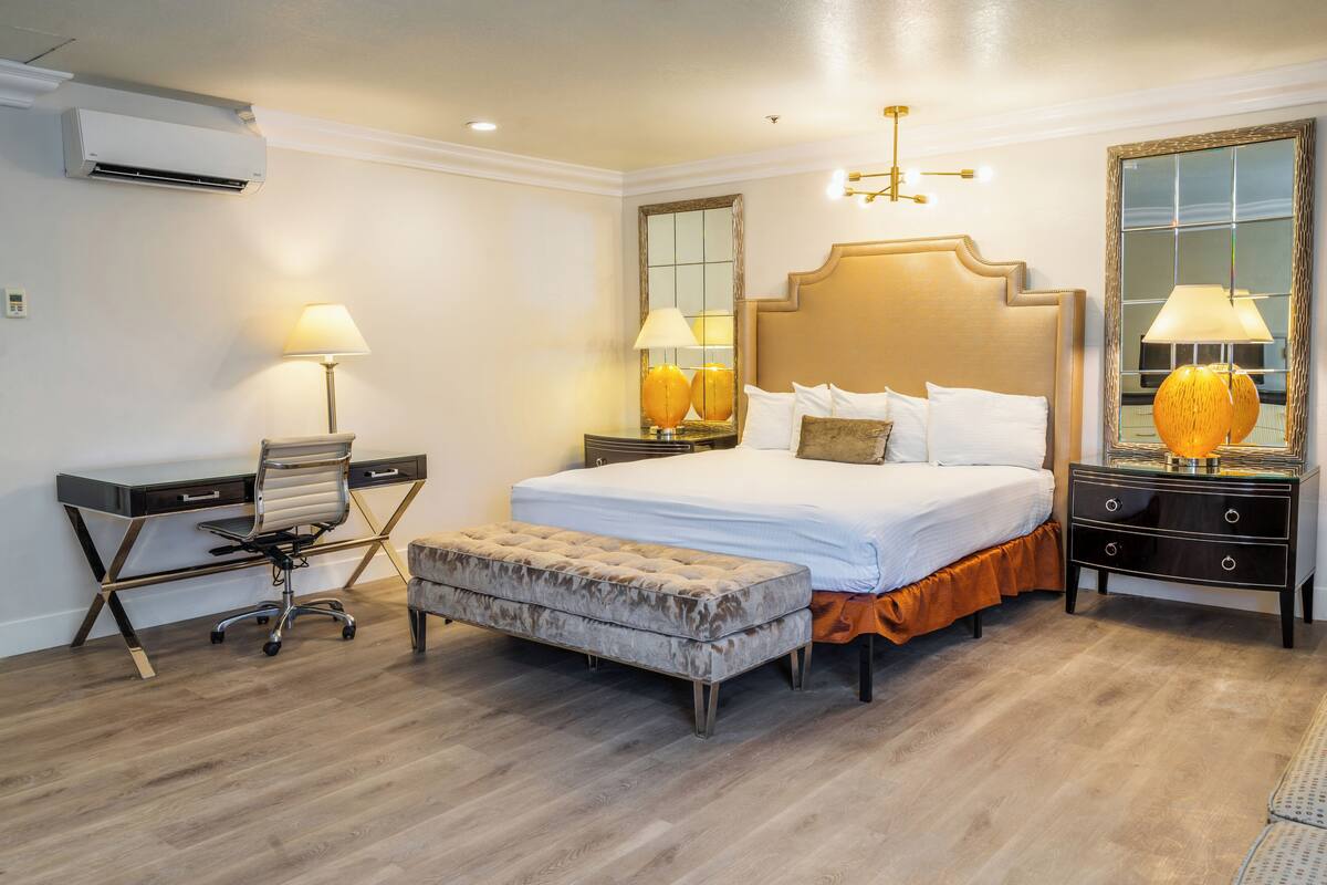 A hotel room with a large bed, a desk, a chair, and a bedside table with lamps.