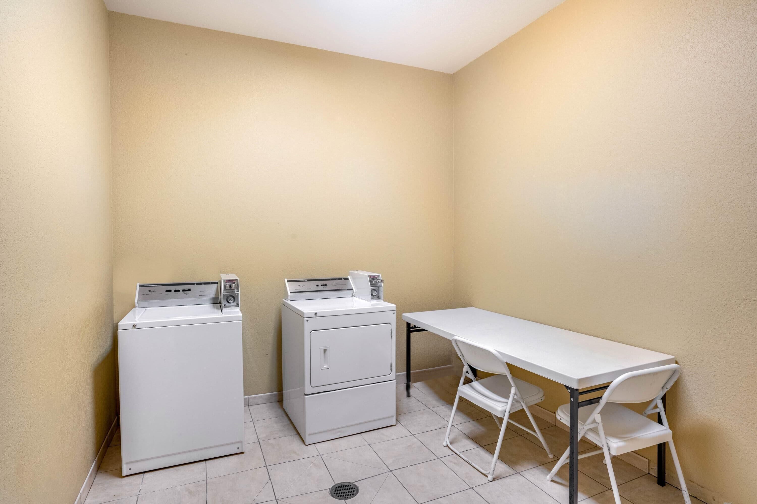 A laundry room with two stacked washers and dryers, a white table, and two chairs.
