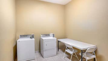 A laundry room with two stacked washers and dryers, a white table, and two chairs.