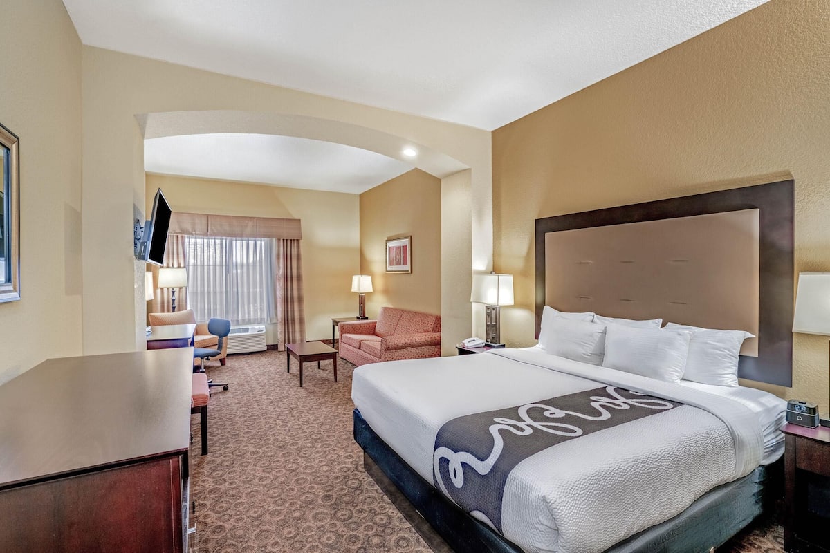 A hotel room with a large bed, a desk, a chair, a TV, and a window with curtains.