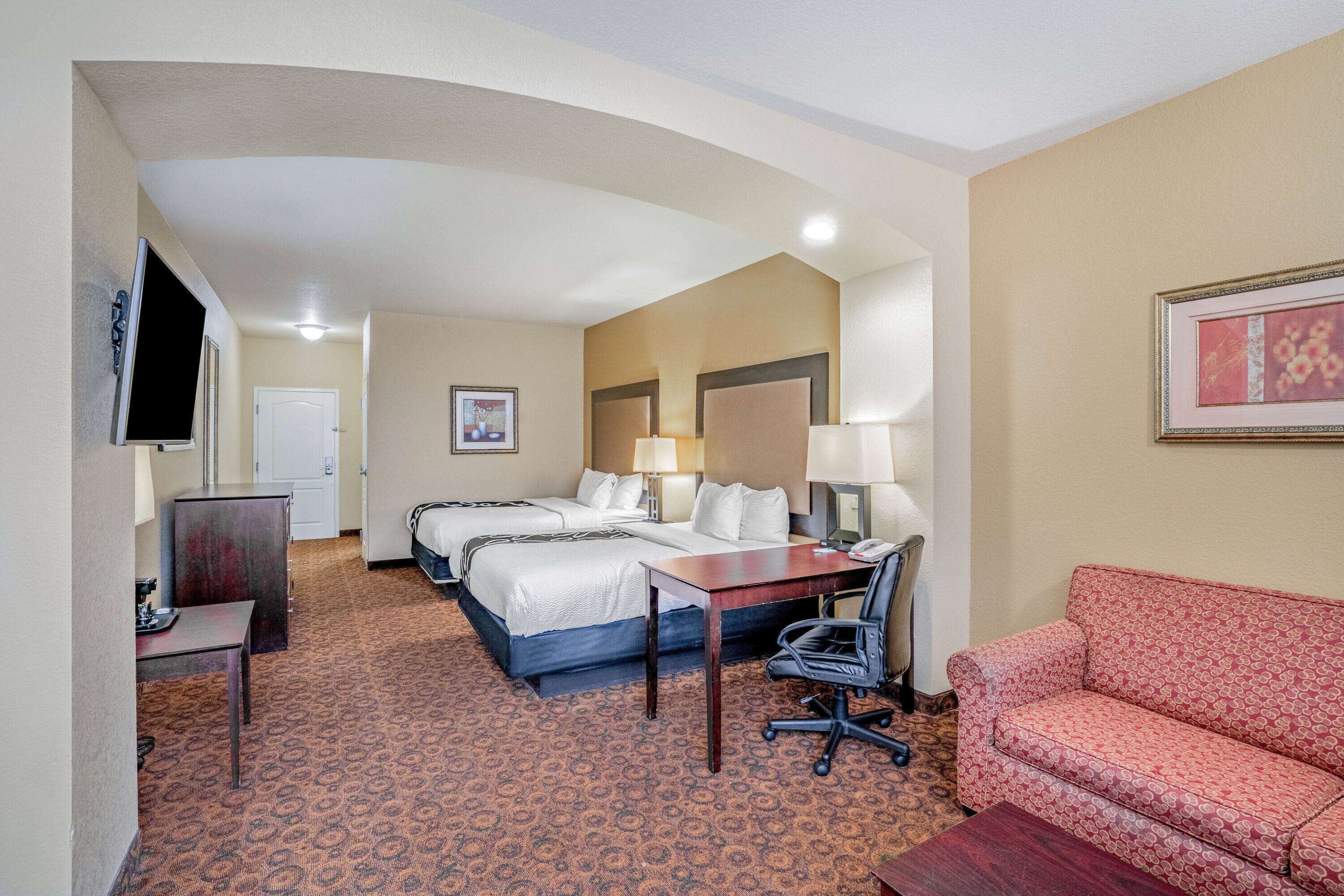 Une chambre d’hôtel avec deux lits, un bureau, une chaise, un canapé et une télévision.